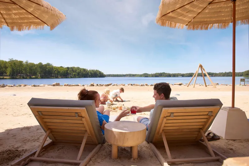  Koppel ontspant op strandstoelen onder een parasol aan het Victoriameer met twee kinderen dat in het zand aan het spelen zijn