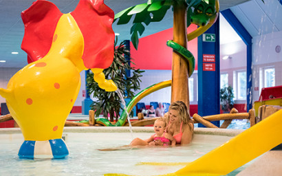 Een moeder speelt met haar dochter in het vrolijke kinderbad, dat is uitgerust met een spuitende olifant en andere speeltoestellen.
