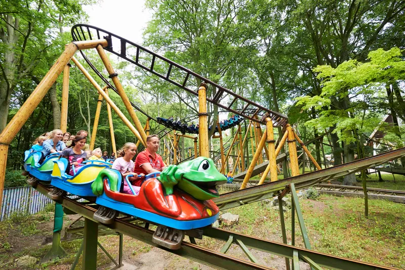 De Kikkerachtbaan in attractiepark Duinrell, een familieachtbaan met een groen kikkertreintje vol met lachende kinderen en ouders, die door een bosrijke omgeving rijdt.
