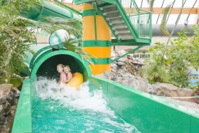 Twee kinderen komen uit groene waterglijbaan in subtropisch zwembad van Landal De Lommerbergen