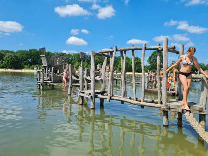 Een meisje klimt op de avontuurlijke houten waterspeeltuin in de zwemvijver van Vakantiepark Witterzomer in Drenthe.