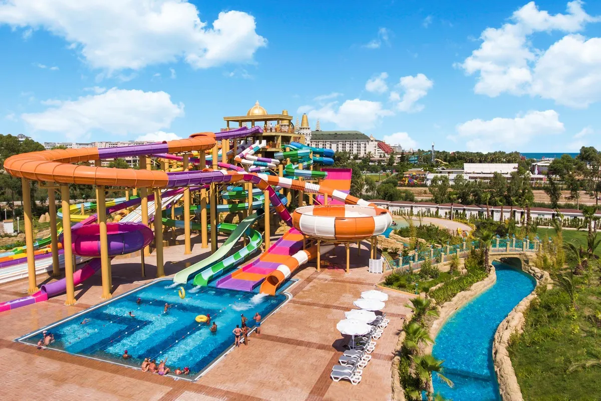 Overzicht van het grote waterpark van Delphin BE GRAND Resort in Lara, met veel kleurrijke glijbanen en een lazy river.
