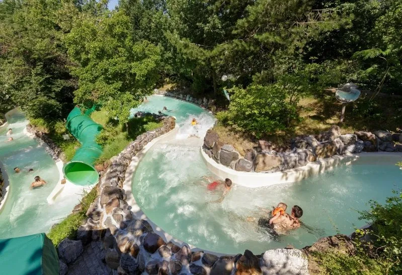 De wildwaterbaan van Aqua Mundo bij Het Meerdal die zich door een groene, bosrijke omgeving slingert, met verschillende mensen in het water.