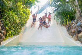 Een lachend gezin met drie kinderen glijdt hand in hand van de brede familieglijbaan in zwemparadijs Aqua Mundo van Center Parcs Het Heijderbos.