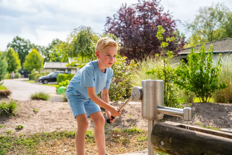 Jongen speelt met een houten waterpomp in de natuurlijke speeltuin van Residence Lichtenvoorde.