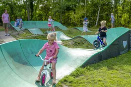 Een kind op een fiets op de golvende pumptrack baan van de camping