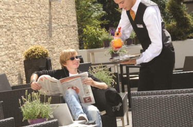 Een jongen ontspant met een krant en een drankje op het gastvrije terras van Parkhotel Oberhausen
