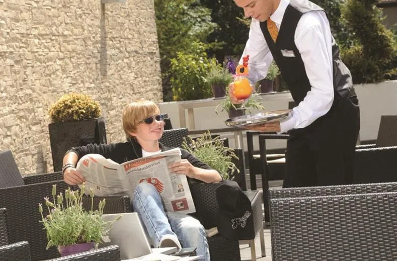 Een jongen ontspant met een krant en een drankje op het gastvrije terras van Parkhotel Oberhausen