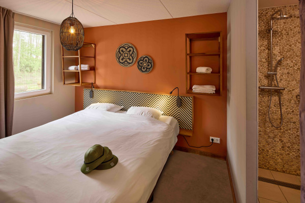 safari-thema tweepersoons slaapkamer in Safari Resort Beekse Bergen met opgemaakt bed en een moderne badkamer met inloopdouche