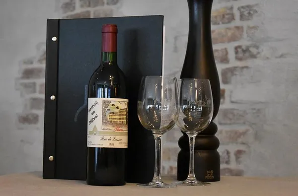 Een fles rode wijn met twee glazen en een menukaart in het restaurant van Hotel Atlanta voor een gastvrij en stijlvol verblijf