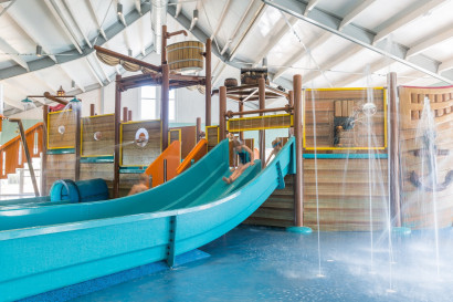 De overdekte waterspeeltuin in de vorm van een schip met een glijbaan in het zwembad van Strandpark De Zeeuwse Kust.