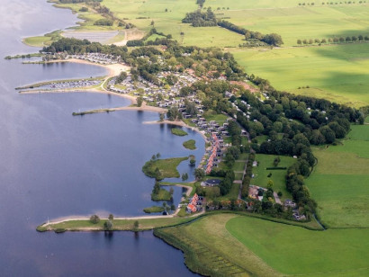 Indrukwekkende luchtfoto van Vakantiepark Bad Hoophuizen, die de unieke ligging direct aan de uitgestrekte kust van het Veluwemeer laat zien.