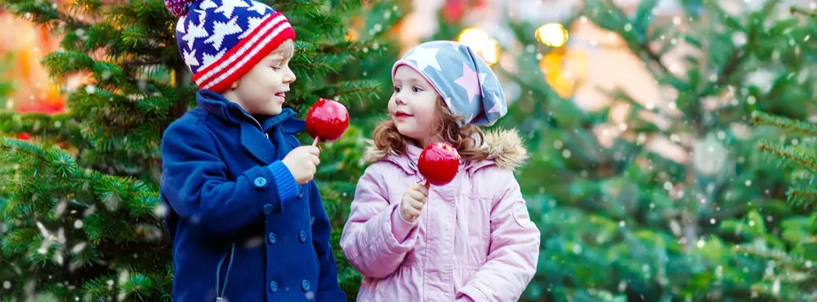 Twee kinderen met kerstkleding eten rode suikerappels voor een kerstboom