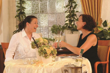 Twee vrouwen proosten met een glas wijn aan een gedekte tafel in het restaurant van Parkhotel Oberhausen