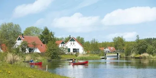 Gezin in een rode kano op het water langs de bungalows van Landal Natuurdorp Suyderoogh, gelegen aan het Lauwersmeer.
