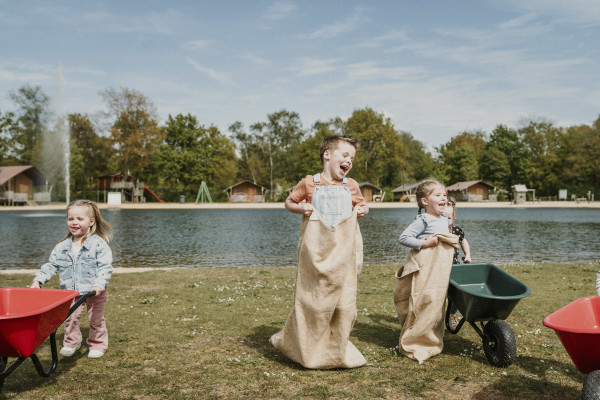 Kinderen spelen zaklopen op grasveld aan strand en zwemvijver Vakantiepark Dierenbos