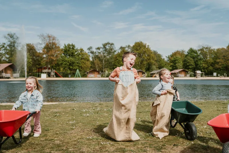 Kinderen spelen zaklopen op grasveld aan strand en zwemvijver Vakantiepark Dierenbos