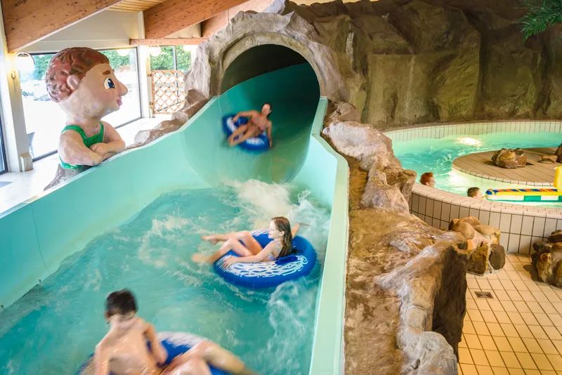 Kinderen komen met opblaasbanden uit een glijbaantunnel en plonzen in het zwembad van Landal Salztal Paradies.