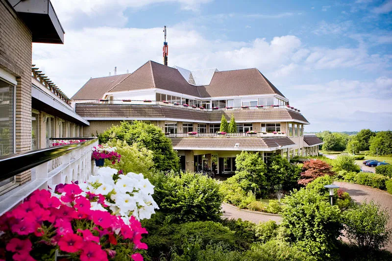 Buitenaanzicht van het kindvriendelijke Van der Valk hotel in Gladbeck, Noordrijn-Westfalen, omgeven door groene tuinen en kleurrijke bloemen.