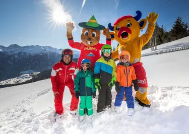 Kinderen staan ion de sneeuw met mascottes op de skipiste