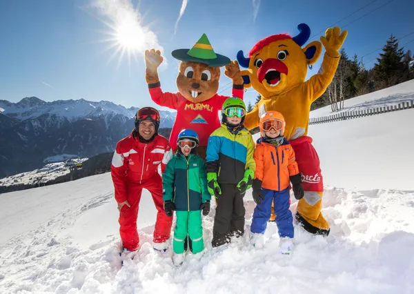 Kinderen staan ion de sneeuw met mascottes op de skipiste