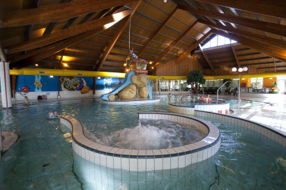 Het overdekte zwembad van Landal Aelderholt met een groot bubbelbad op de voorgrond en een waterglijbaan en stroomversnelling op de achtergrond.
