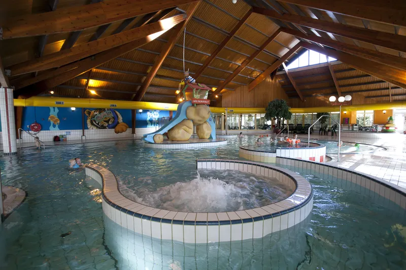 Het overdekte zwembad van Landal Aelderholt met een groot bubbelbad op de voorgrond en een waterglijbaan en stroomversnelling op de achtergrond.