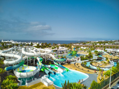 Panoramisch overzicht van het Aqualava Waterpark met talloze glijbanen en zwembaden, met op de achtergrond de kustlijn en de zee van Lanzarote.