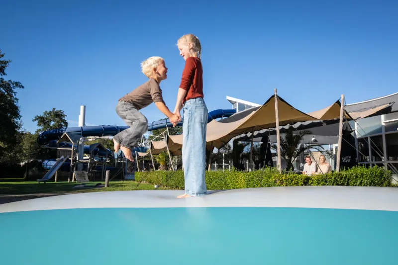 Twee kinderen springen hand in hand op de grote airtrampoline op Kustpark Texel.