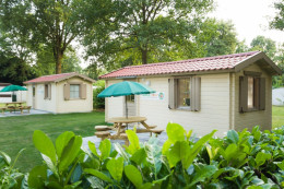 Een simpel chalet huisje met een picknick tafel en groene parasol.