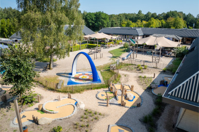 Overzicht van de centrale buitenspeeltuin en het terras bij Bospark Lunsbergen, met diverse speeltoestellen, zand en een interactieve Sona dansboog.