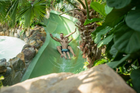Een vader en zoon glijden lachend samen van de brede, groene waterglijbaan in de tropische Aqua Mundo van Center Parcs Het Meerdal.