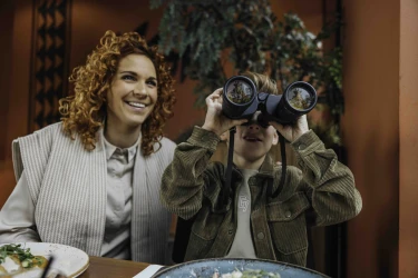 Moeder en kind aan tafel en kind kijkt door verrekijker tijdens diner in Safari Resort Beekse Bergen