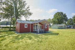 Een rood gekleurd luxe challet huisje met veranda  op een groen grasveld.