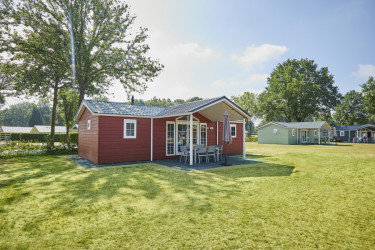 Een rood gekleurd luxe challet huisje met veranda  op een groen grasveld.