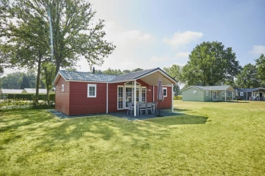 Een rood gekleurd luxe challet huisje met veranda  op een groen grasveld.