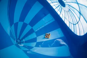 Een groep mensen in een gele opblaasbare band glijdt door de gigantische, blauw-wit geblokte trechter van de waterglijbaan Saltato in het zwemparadijs van Landal Hof van Saksen.