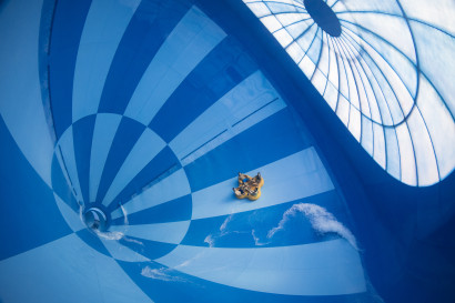 Een groep mensen in een gele opblaasbare band glijdt door de gigantische, blauw-wit geblokte trechter van de waterglijbaan Saltato in het zwemparadijs van Landal Hof van Saksen.