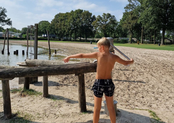 Kind speelt bij waterspeeltuin op het strand van Recreatiepark De Leistert aan de zwemvijver
