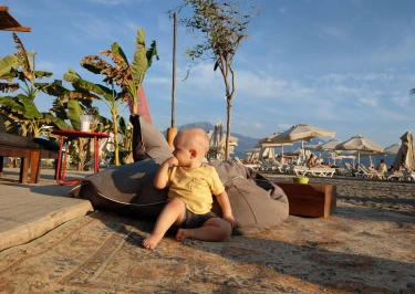 Baby zit op zitzak aan het strand vol palmbomen