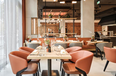 Het moderne restaurant met oranje en grijze tinten van ATLANTIC Hotel Münster en gedekte tafels 