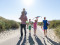Een vrolijk gezin met drie kinderen wandelt met een vlieger door de duinen op weg naar het strand van Texel, vlak bij Landal Vogelmient.