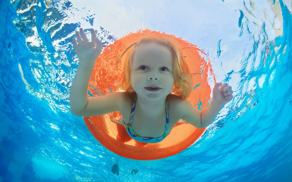 Meisje zwemt onder water door een oranje zwemband in een zwembad