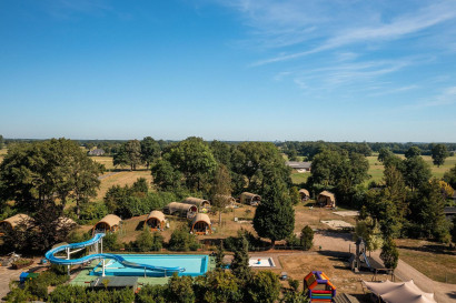 Een luchtfoto van Vakantiecentrum 't Schuttenbelt in Twente, met het grote buitenzwembad met waterglijbaan en de lodges in een groene omgeving.