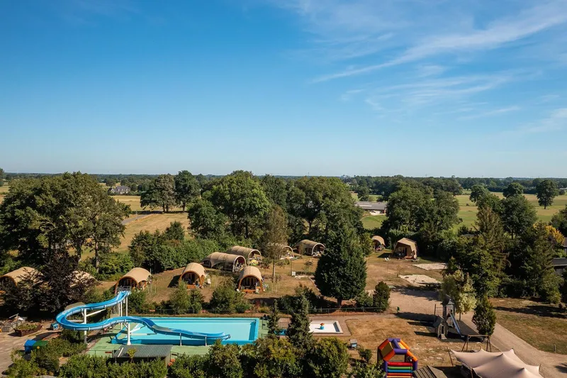 Een luchtfoto van Vakantiecentrum 't Schuttenbelt in Twente, met het grote buitenzwembad met waterglijbaan en de lodges in een groene omgeving.