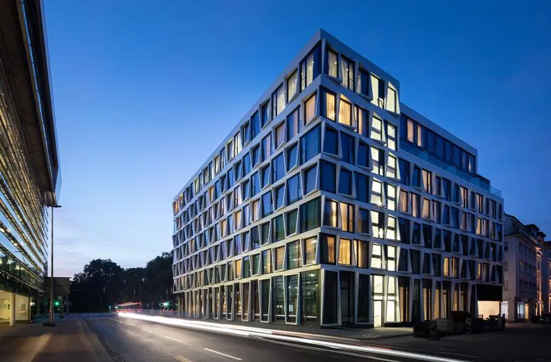 Het moderne exterieur van het ATLANTIC Hotel Münster in de avond, met sfeervol verlichte ramen, centraal gelegen in de stad.