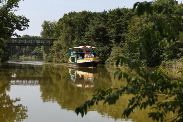 De safariboot vaart met bezoekers over het water langs de groene oevers van Beekse Bergen
