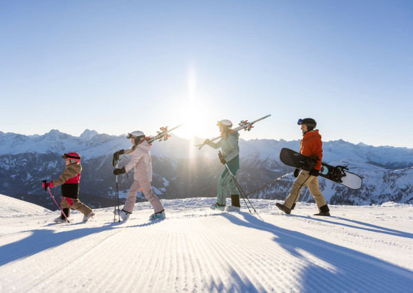 Gezin loopt op de piste tijdens zonsondergang met ski's op hun schouder