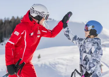 Kind staat op de skipiste en geeft high five aan skileraar