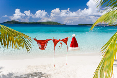 Rode bikini en kerstmuts hangen aan een lijn tussen palmbomen op een tropisch strand met turquoise water